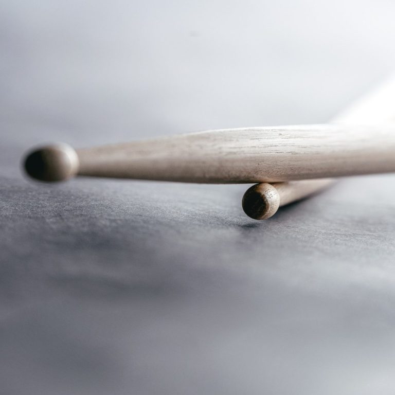 Sticks auf Snare Zwei Drumsticks liegen auf einer dunklen Oberfläche, einer leicht über dem anderen.
